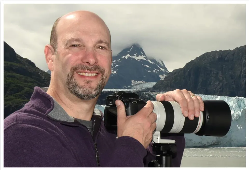 Brad Balfour holding a camera while hiking in the mountains.